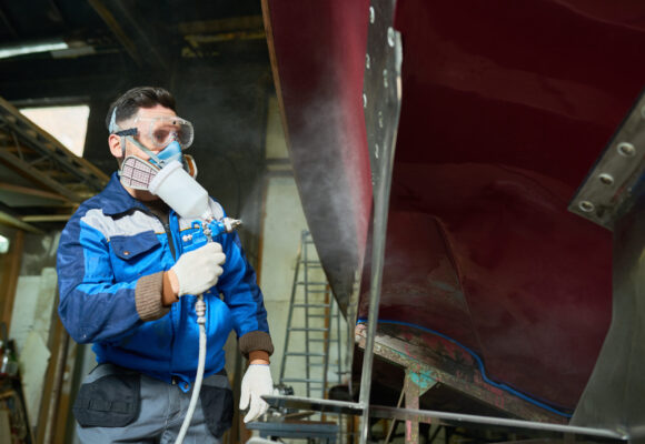 Low angle portrait of unrecognizable worker wearing protective mask painting boat using paint sprayer in yacht workshop, copy space